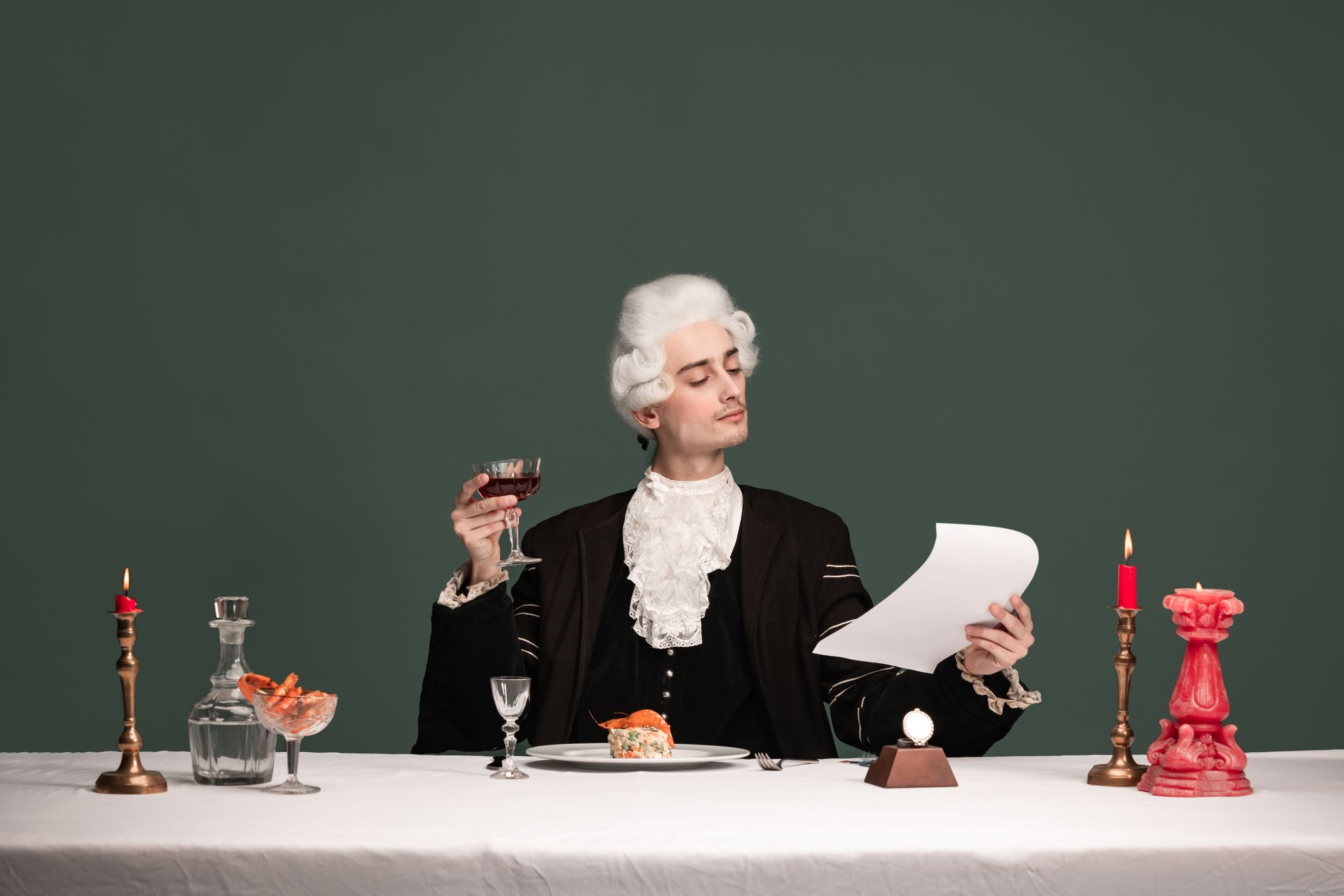 Création d'un chef-d'oeuvre. Portrait de jeune homme élégant en pérou et vintage assis à la table isolée sur fond vert foncé.